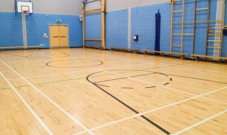 Wooden sports flooring in gym with basketball court markings.