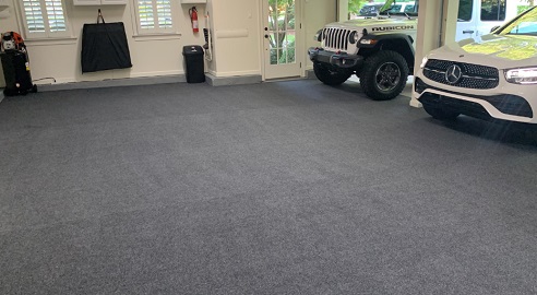 Garage with carpet-style grey flooring and parked cars